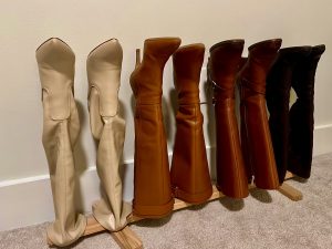 Wooden dowel rack neatly organizing six pairs of tall women's boots in varying shades of beige, brown, and black. The boots are held upright against a neutral-colored wall on a carpeted floor, showcasing a functional and stylish boot storage solution.