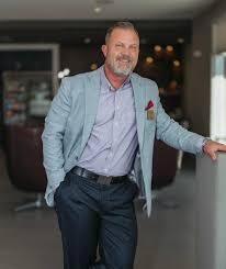 Tony Bagnano standing indoors, wearing a blazer and smiling in a professional setting